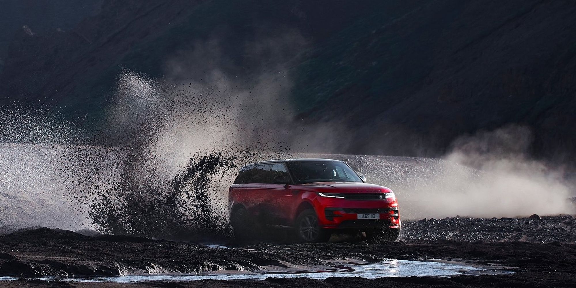 Front 3/4 view of a red Range Rover Sport sliding on wet sand