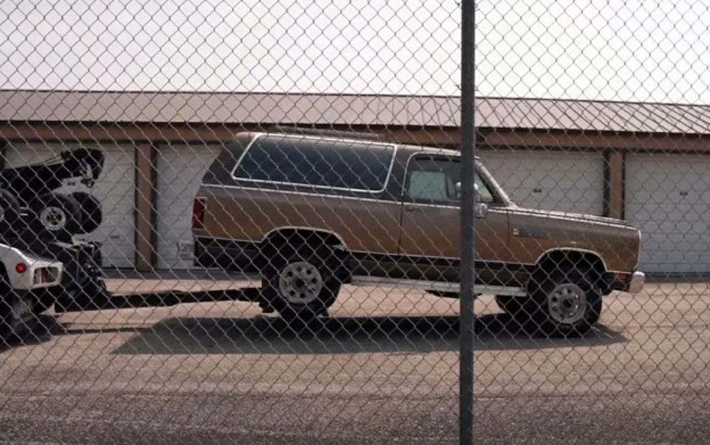 A brown-bronze 1989 Dodge Ramcharger, side profile from other side of fence
