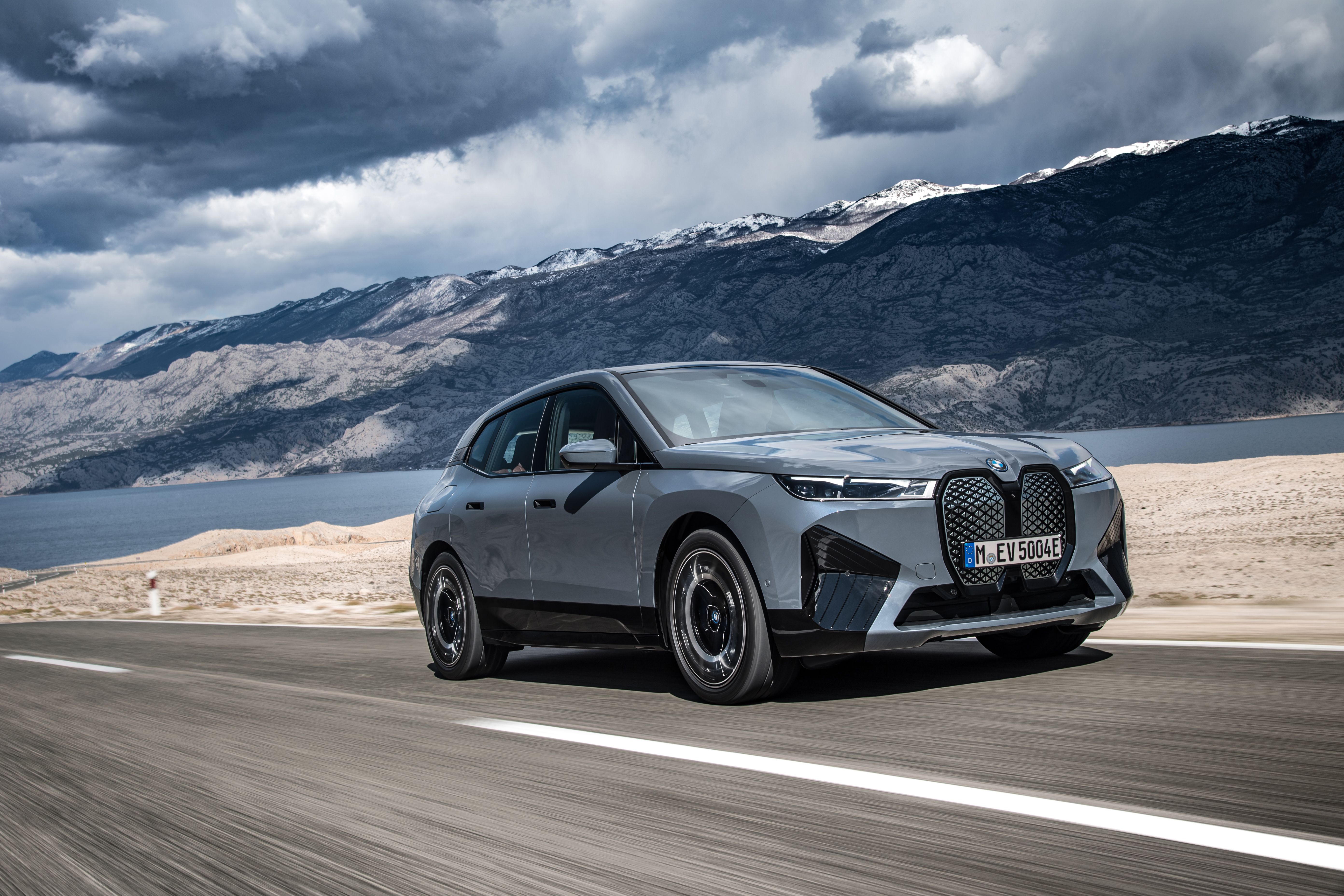 The BMW iX xDrive50 speeds up on the road, front, mountains