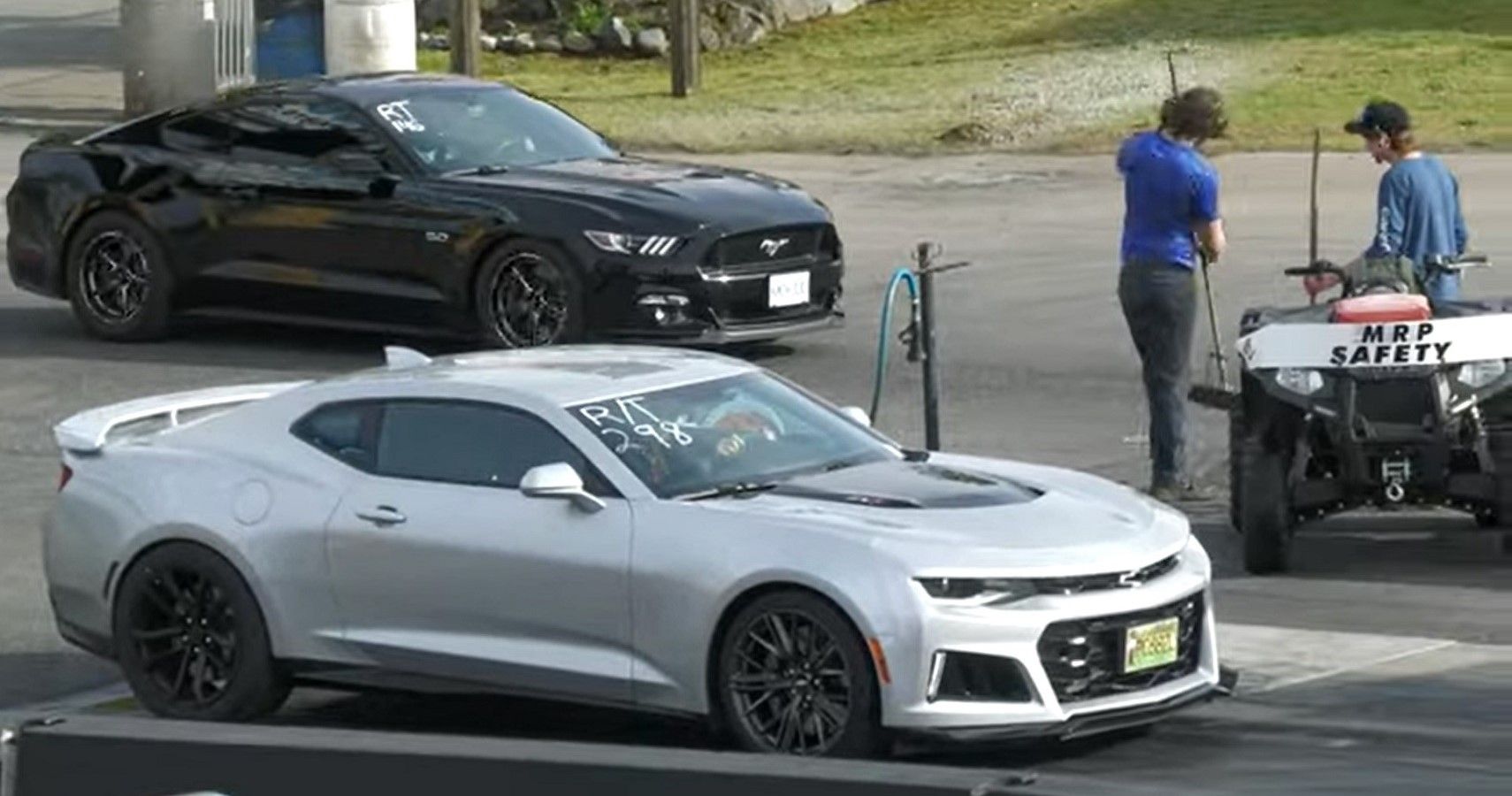 Drag race between Ford Mustang GT and Chevrolet Camaro ZL1, side by side, front quarter view on drag strip