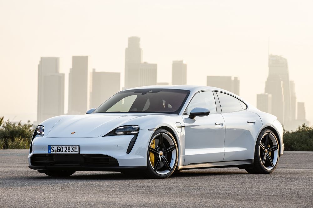 A white Porsche Taycan three-quarter view foregrounding a sunset