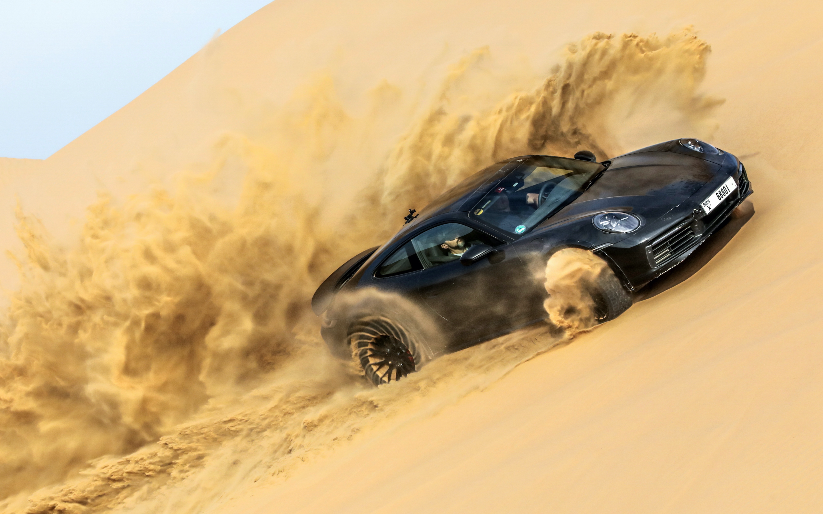 Black 2023 Porsche 911 Dakar Driving Up A Desert Dune