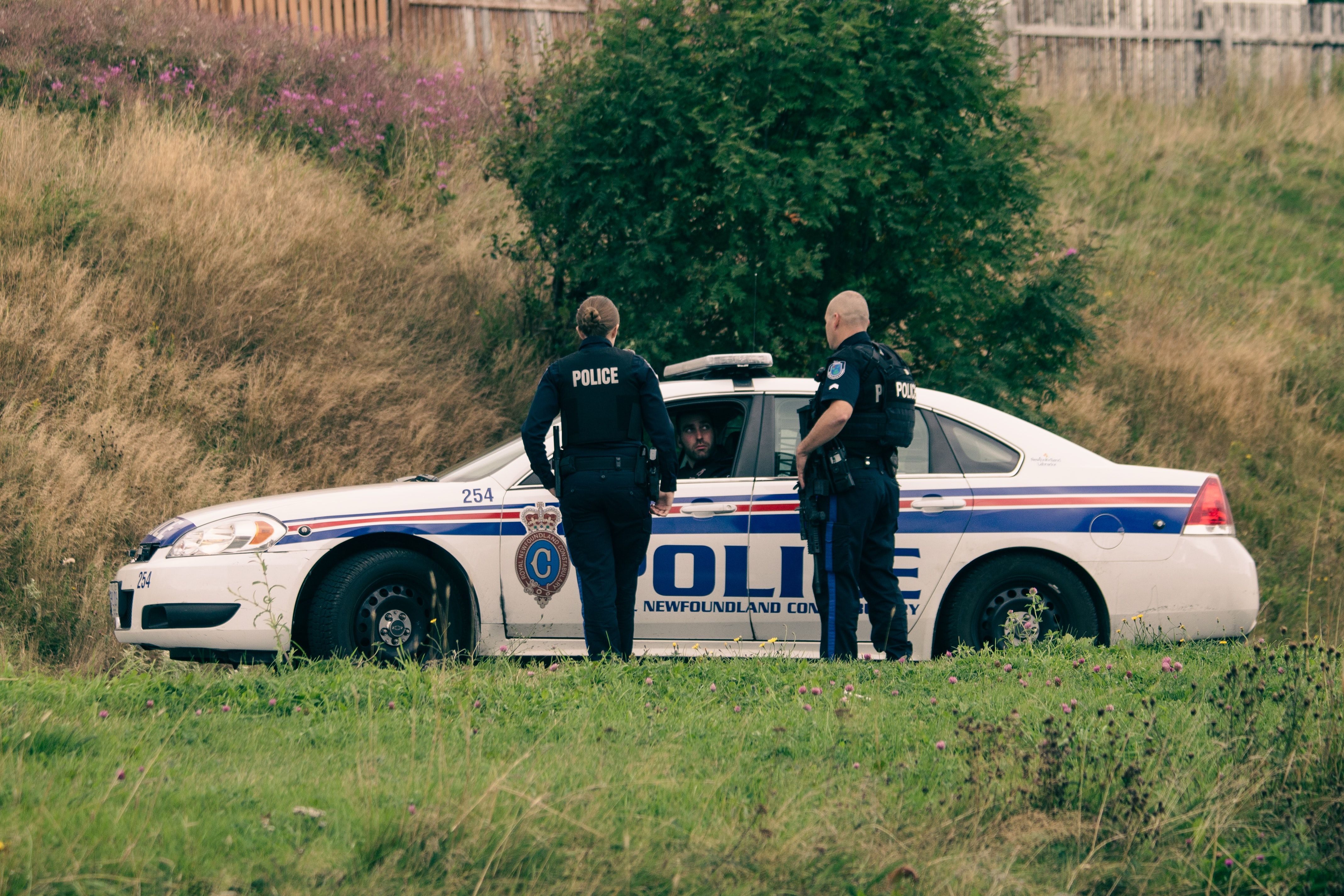 Three police officers talk by their car. 