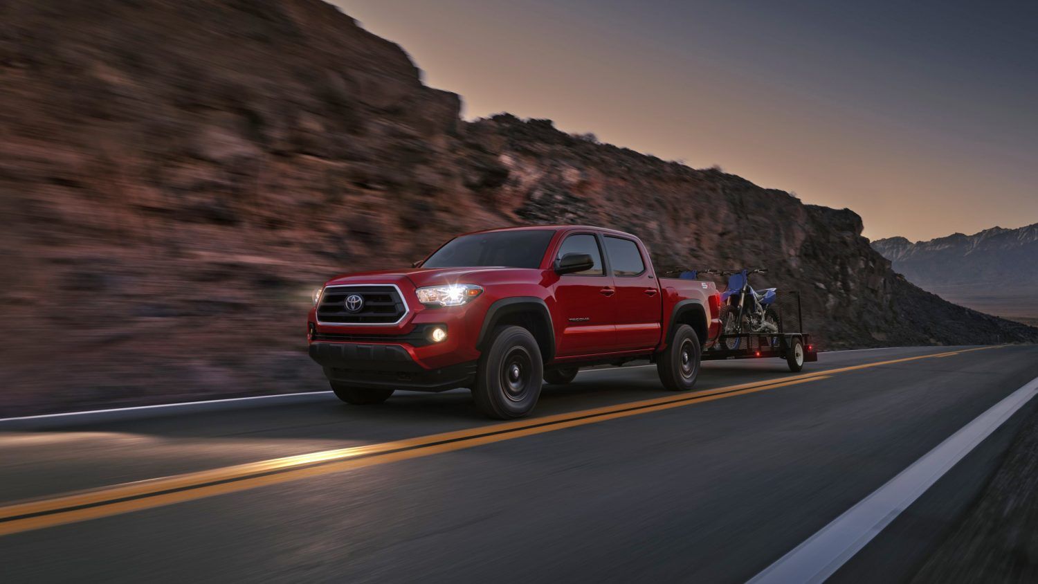 red 2023 Toyota Tacoma driving down the highway in the evening