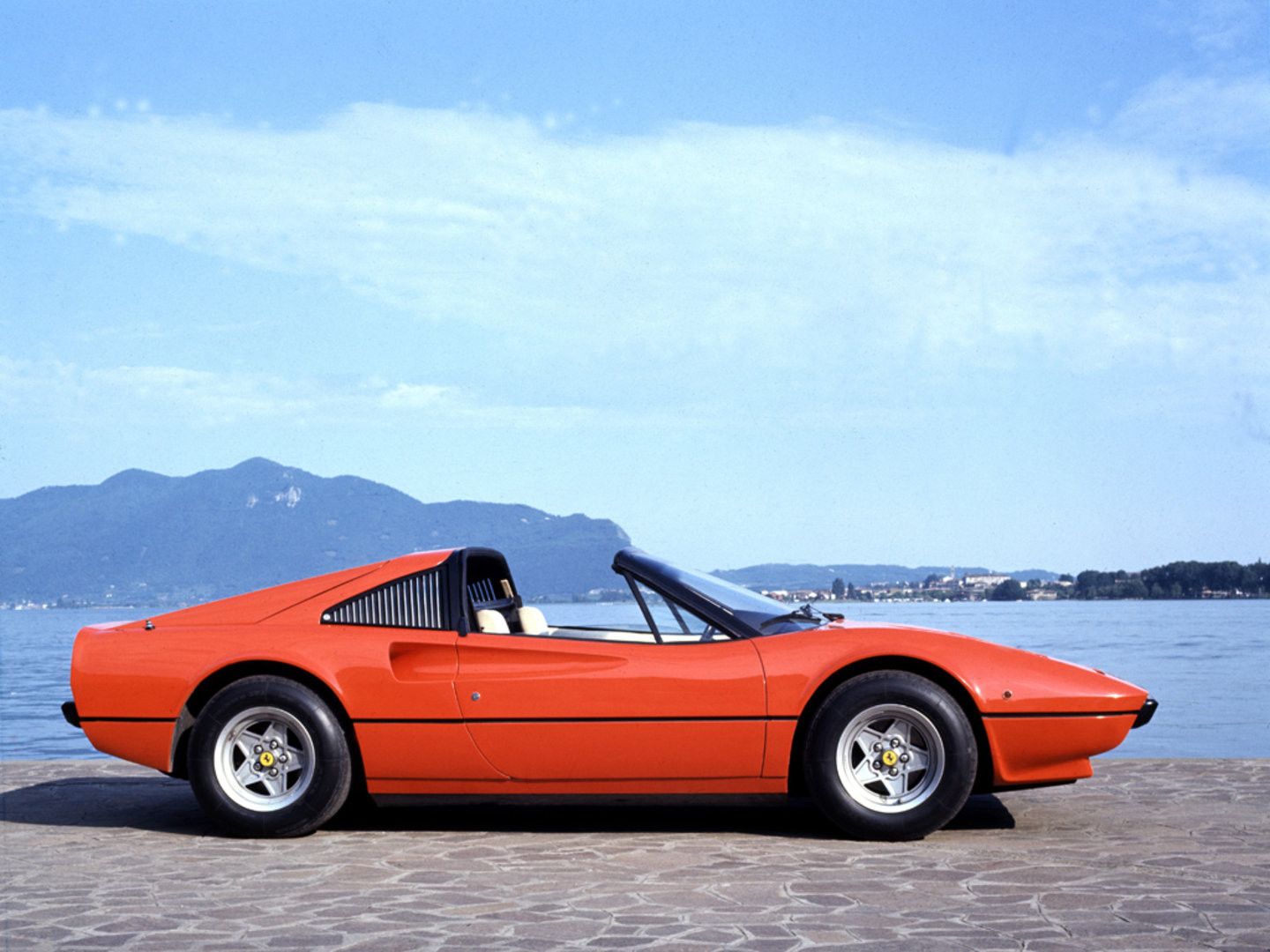 red ferrari 308 gts with a cream leather interior parked sideways next to a mountain and a lake
