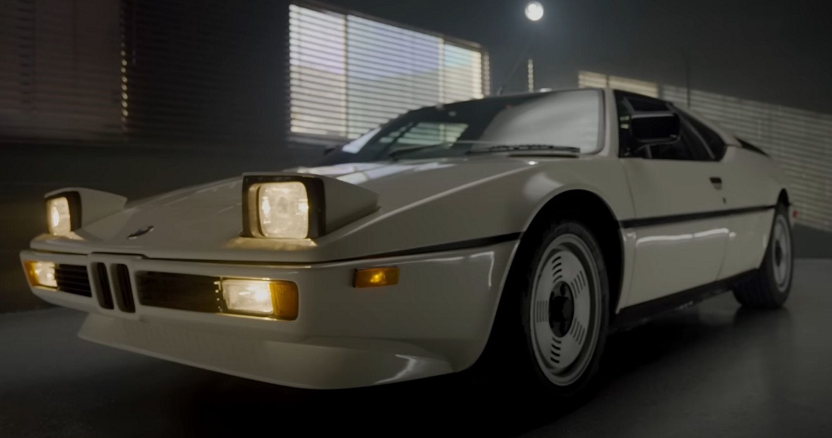 A BMW M1 in white with illuminated headlights