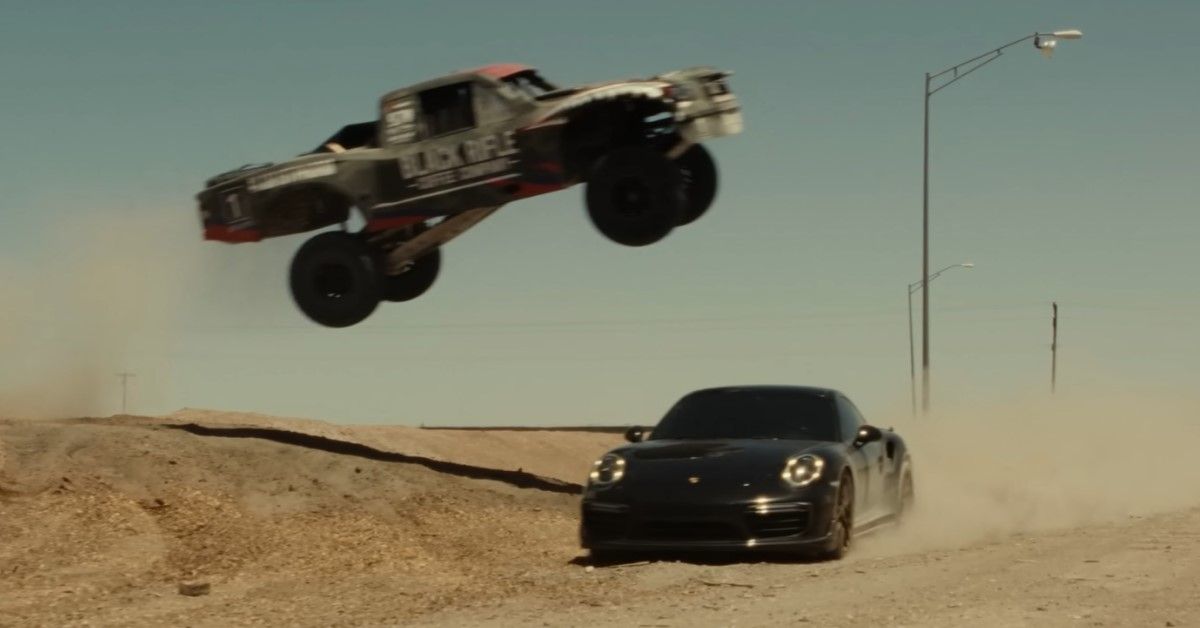 A Trophy truck flying over a Porsche 911 Turbo S