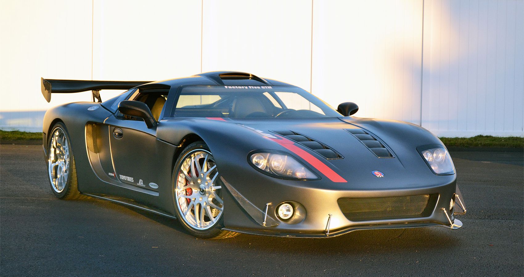 A black and red Factory Five GTM Supercar modeling outside.