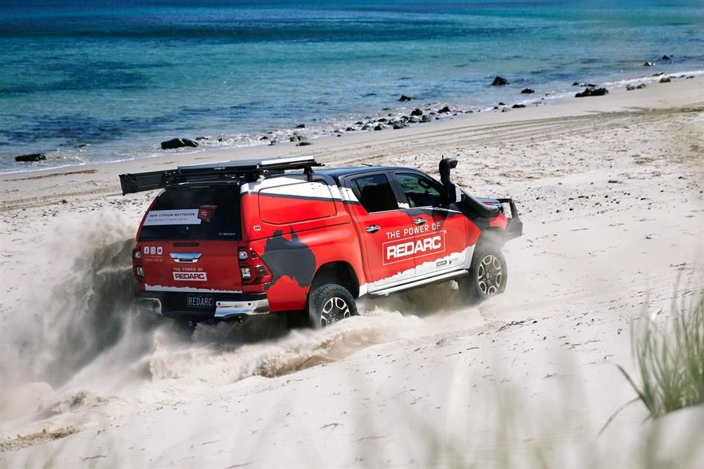 Red custom built 2020 Toyota Hilux driving on the beach