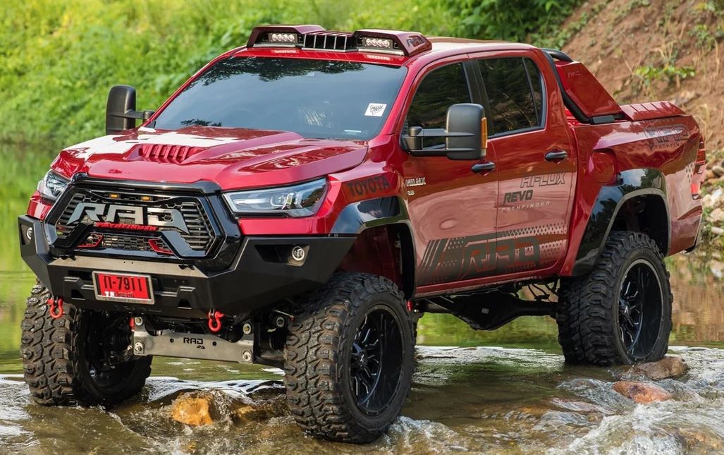 Red custom built Hilux driving through river