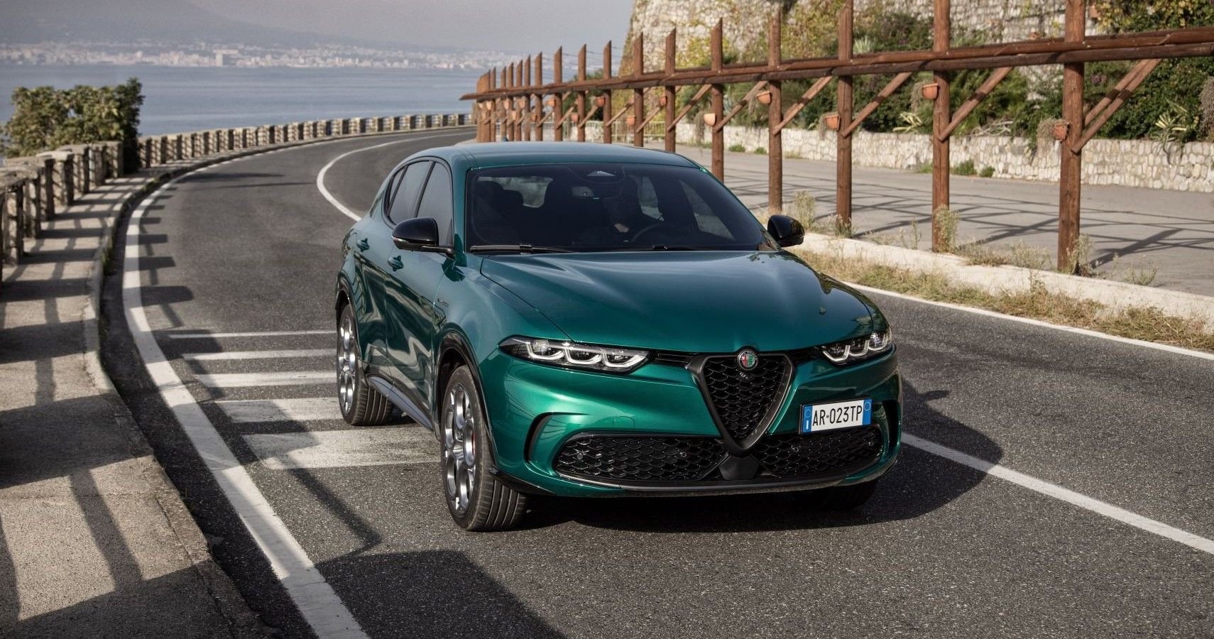 A green Alfa Romeo Tonale 2024 on a seaside road with a view of the third quarter