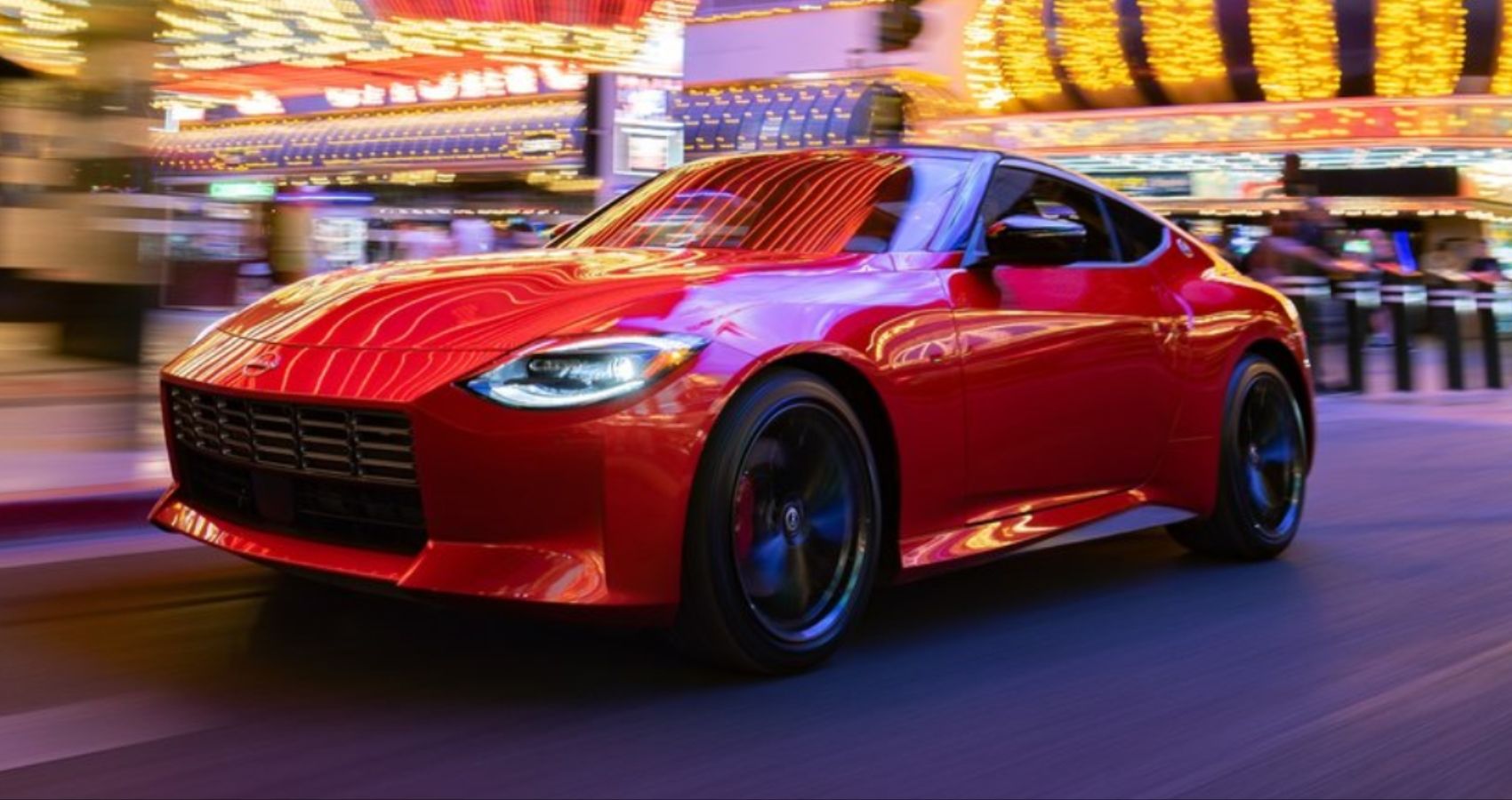A 2023 Nissan Z Driving A Night In The Center Of A City In A Deep Red Color