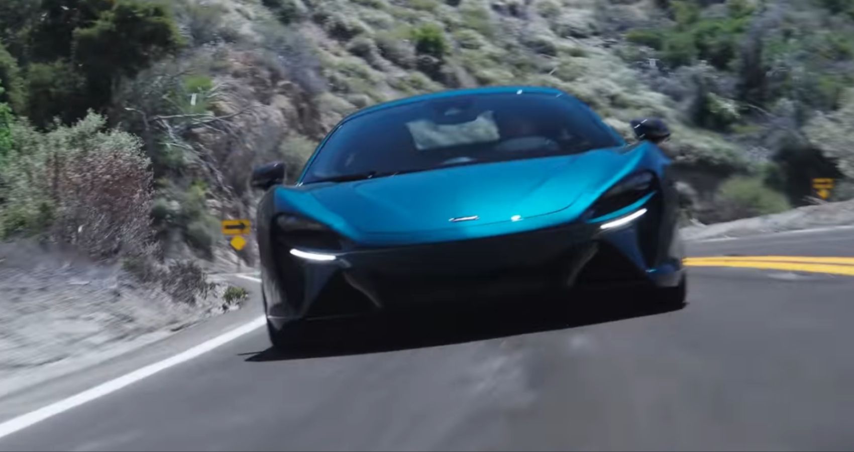 McLaren Artura Throttle House Front Quarter View em movimento em uma estrada sinuosa