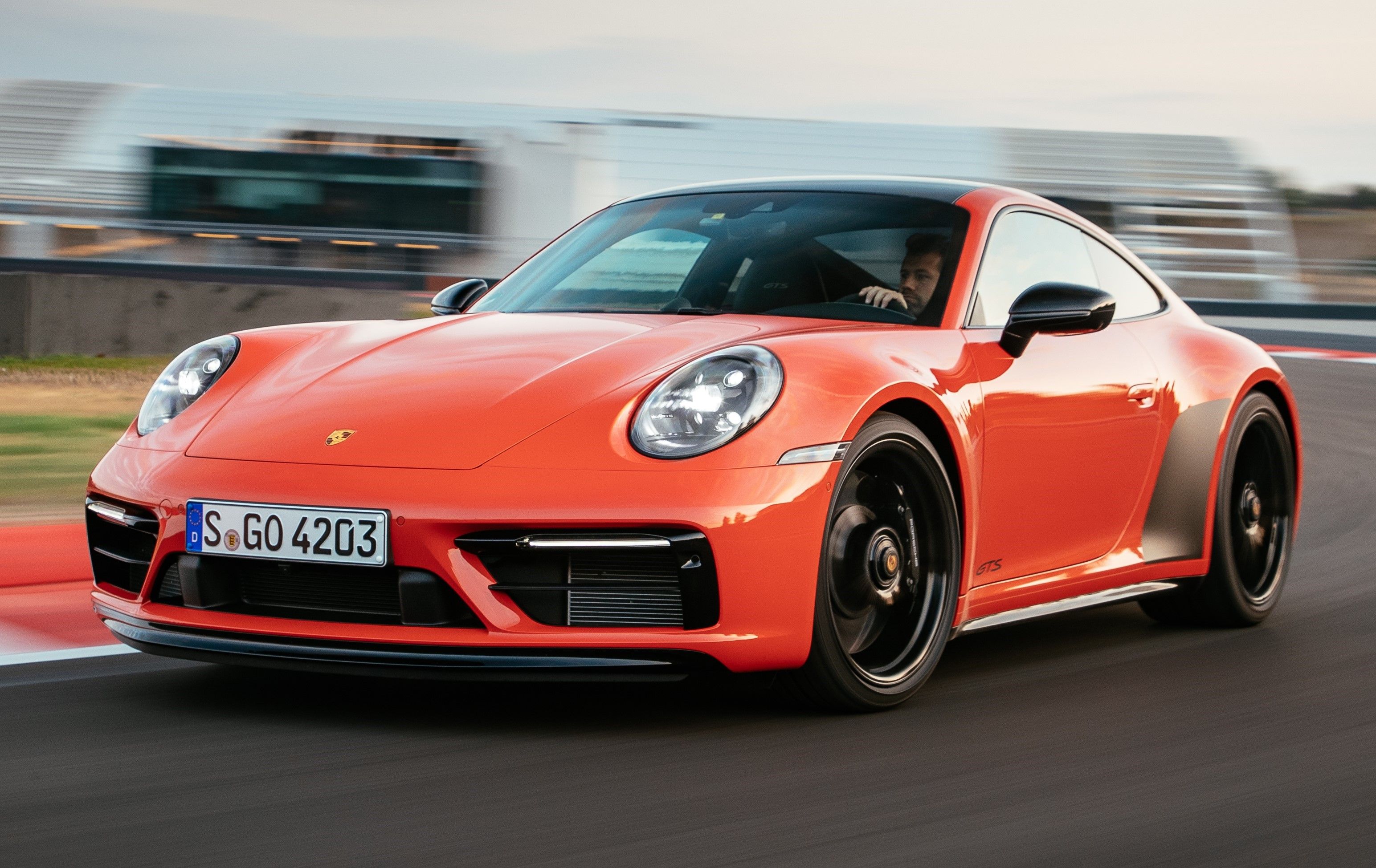 Orange 2023 Porsche 911 Carrera 4 GTS driven on the track