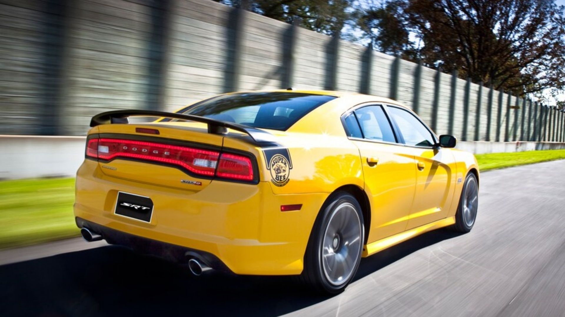 Dodge Charger Super Bee 2012 em amarelo com detalhes em preto em uma pista de corrida ao lado de uma cerca.