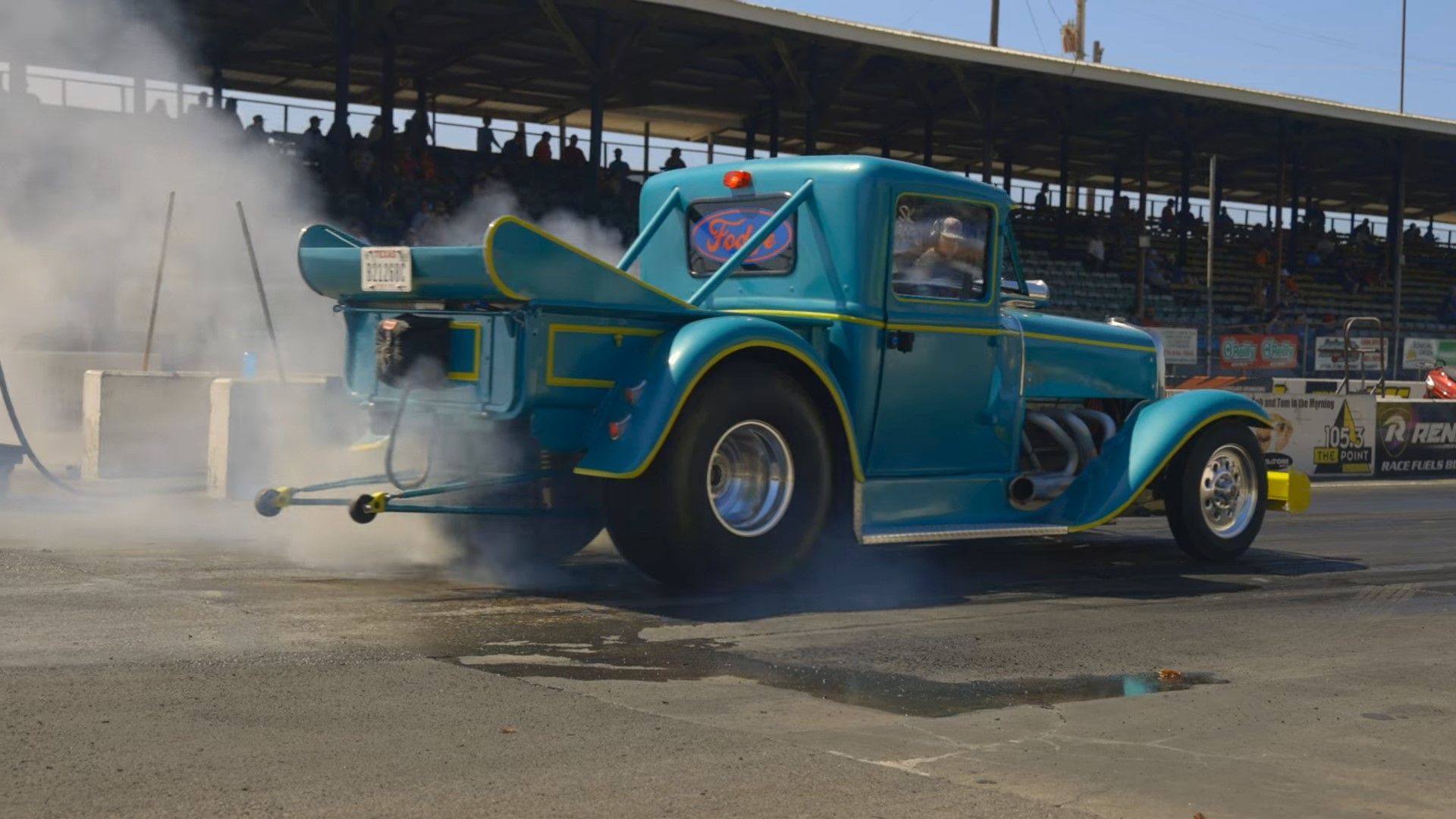 A blue and yellow 1929 Ford Model A Drag Car doing a burnout rear quarter shot