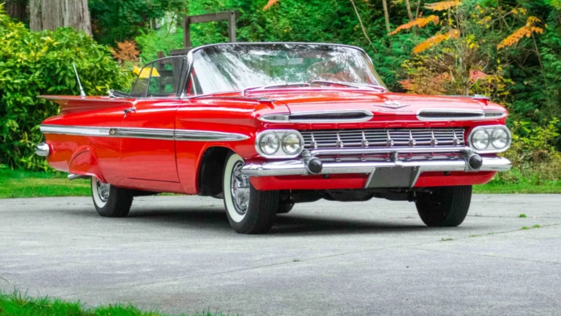 Chevrolet Impala 1959 conversível equipado com Tri-Power em vermelho com detalhes cromados em um estacionamento perto de árvores.