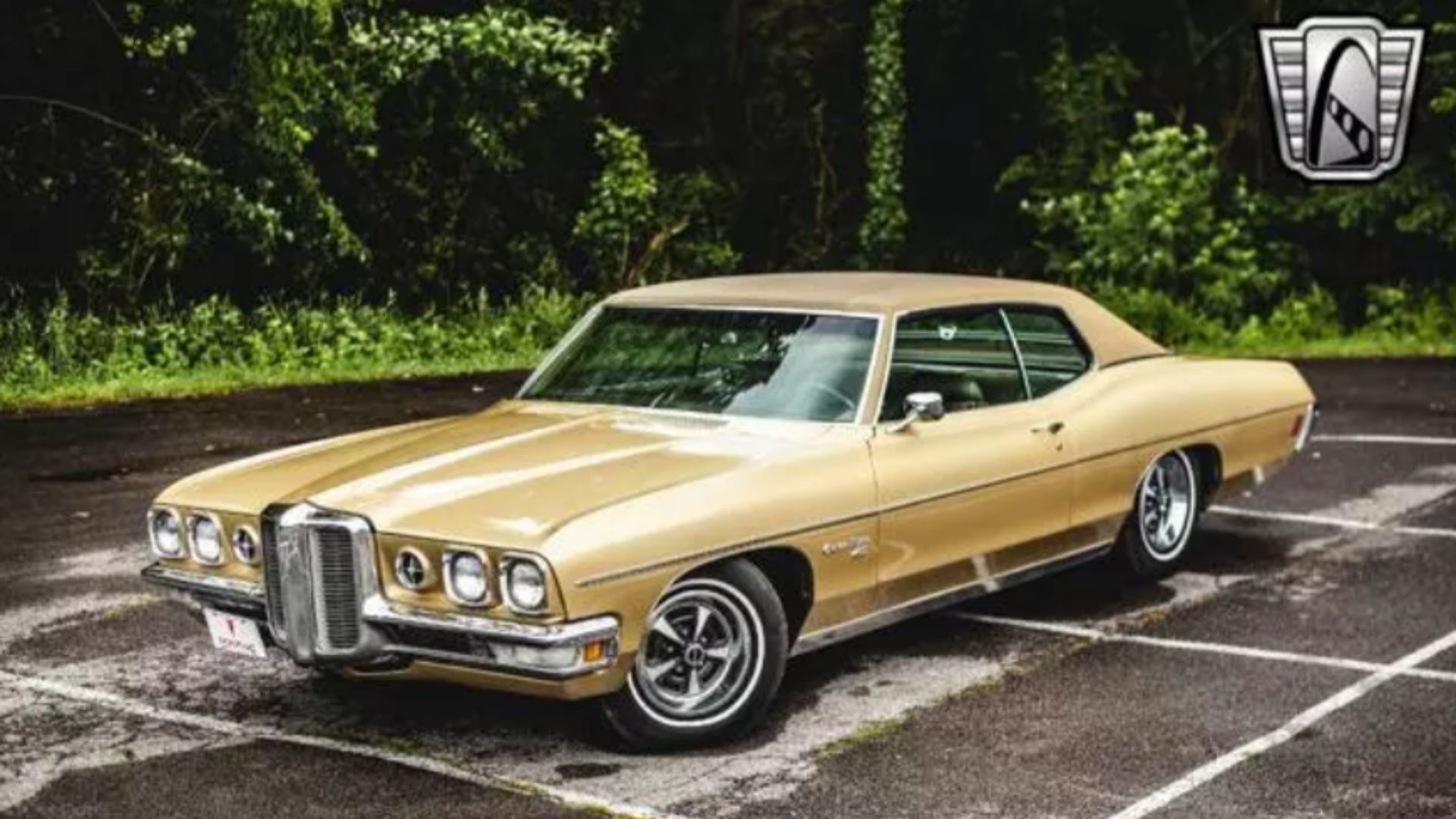 1970 Pontiac Catalina em amarelo com rodas cromadas em um estacionamento e fundo de árvore.