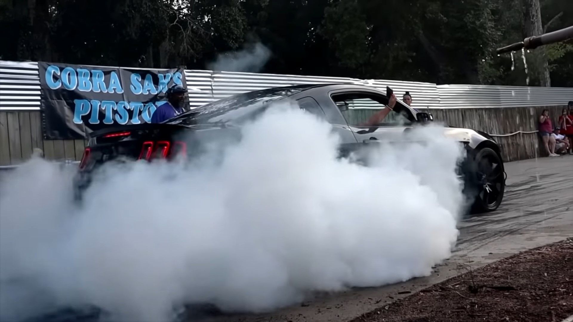 A black 2012 Ford Mustang GT doing a burnout rear quarter shot