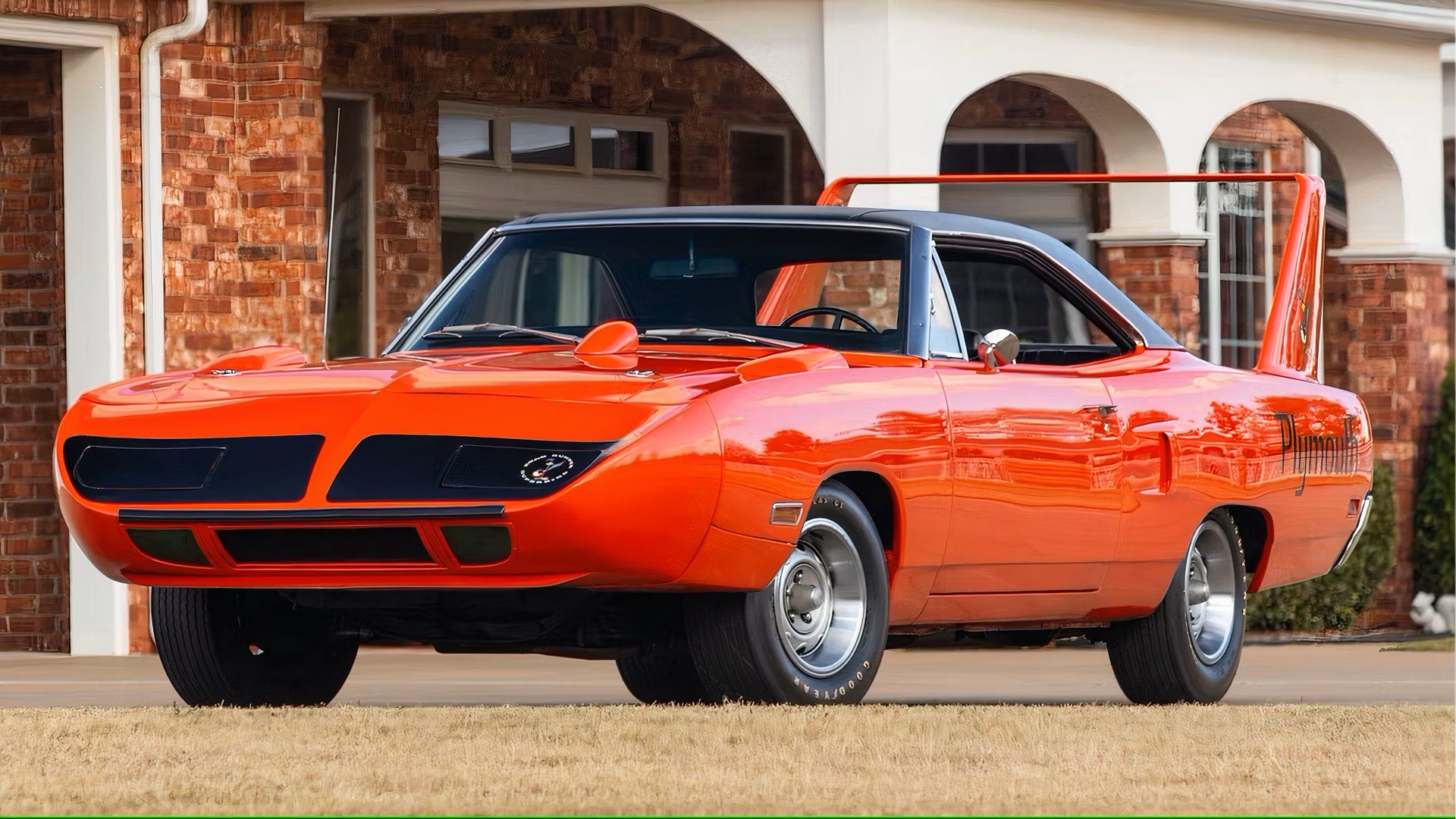 Plymouth Superbird 1970 em laranja com asa laranja e capota cinza em frente a um prédio.