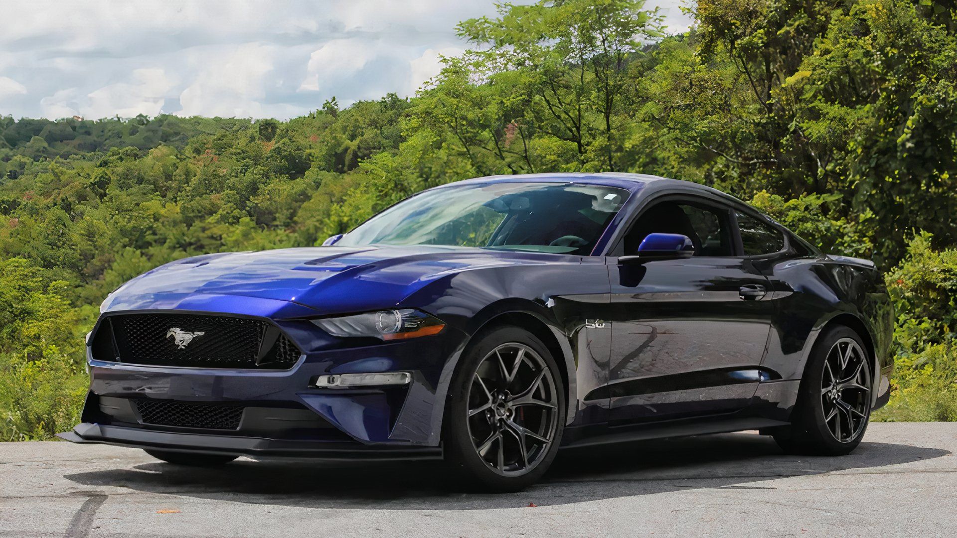 2019 Ford Mustang GT Blue com rodas cinzentas em frente às árvores.