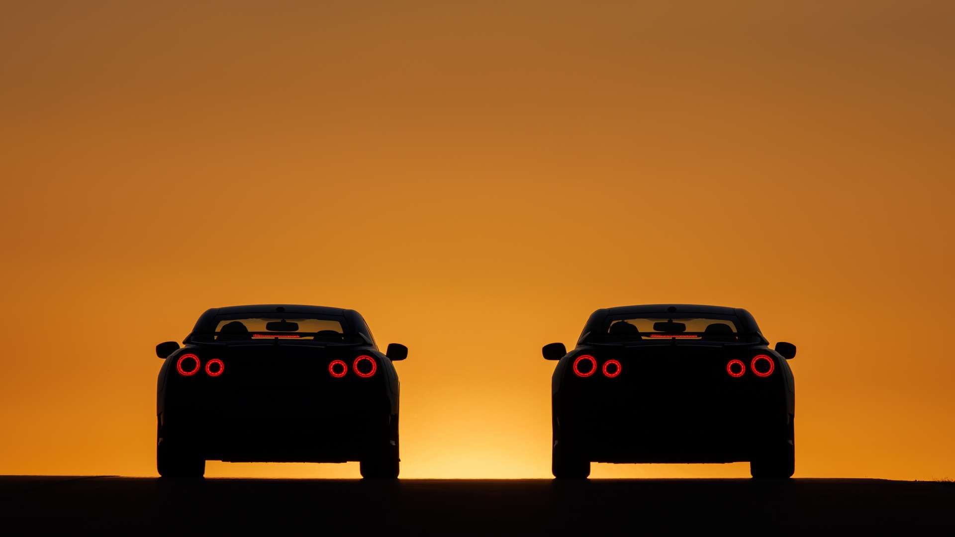 Dois modelos GT-R voltados para o pôr do sol em silhueta