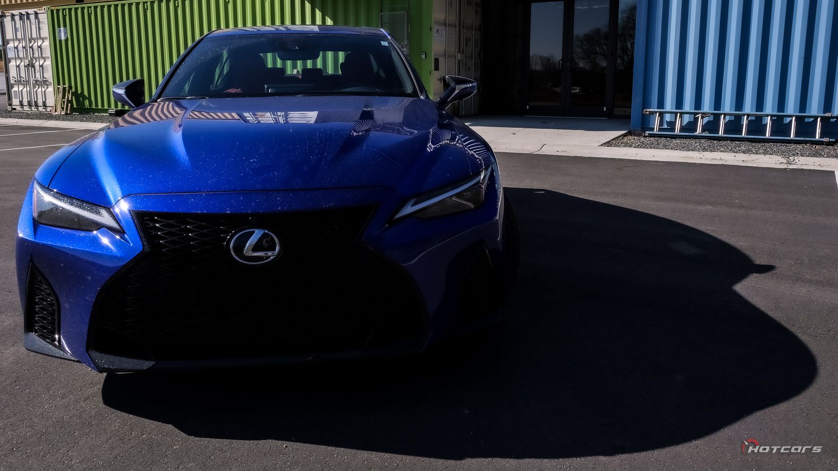 Снимок передней части Lexus IS500 F Sport 2023 года рядом с транспортными контейнерами
